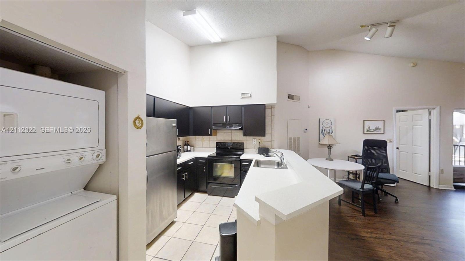 Kitchen featuring dark cabinetry, stainless steel appliances, ceramic tile flooring, a peninsula with counter seating, and vaulted ceilings