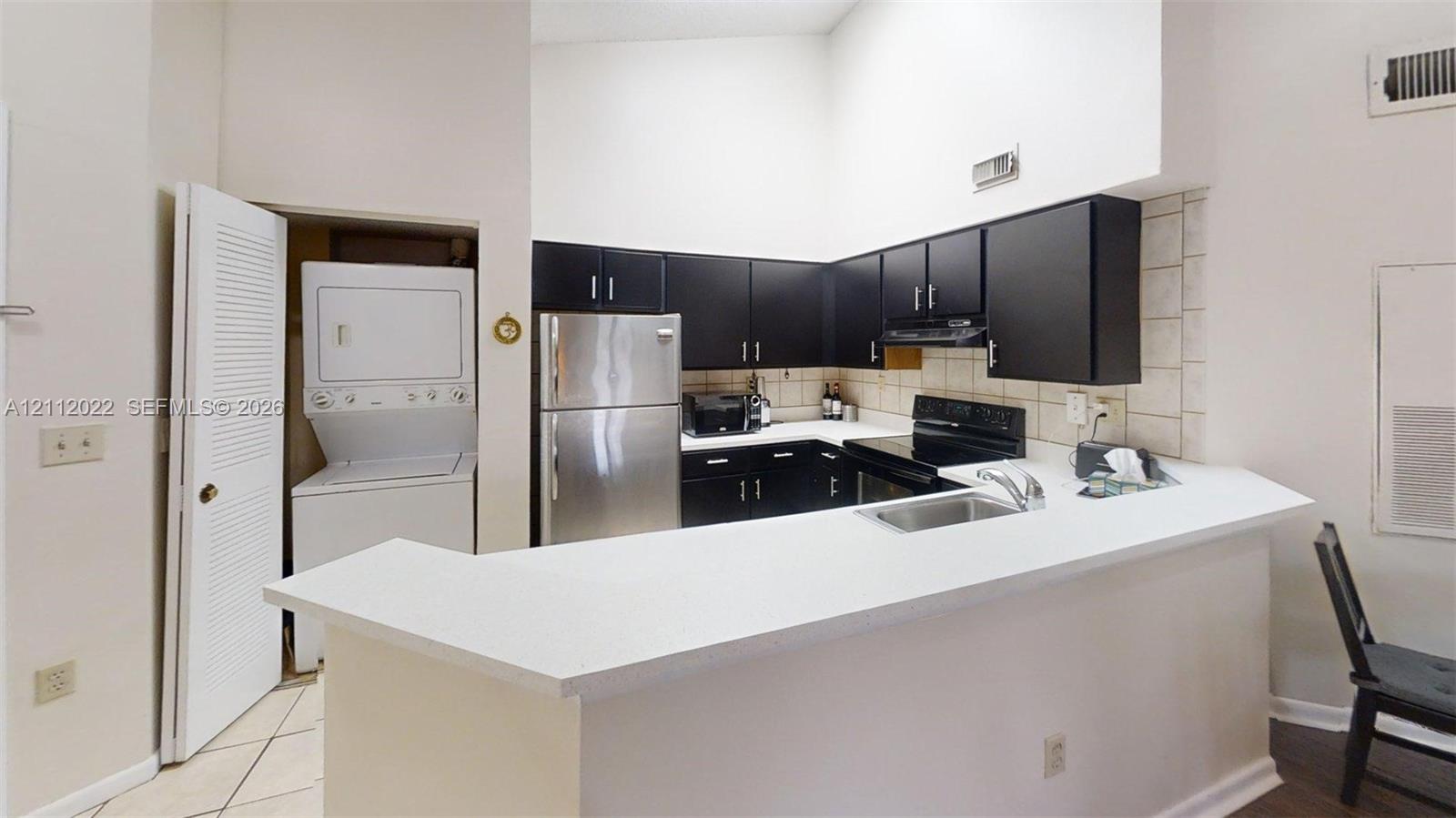 Kitchen featuring dark cabinetry, solid-surface countertops, stainless steel appliances, a recessed stainless steel sink, and a high-vaulted ceiling