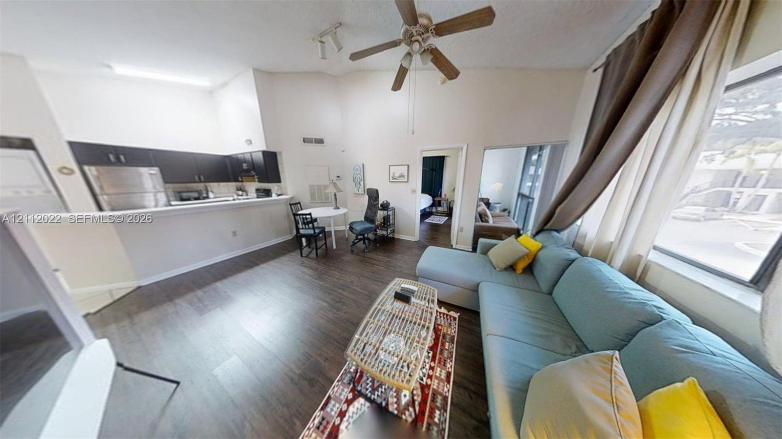 Open-concept interior featuring vaulted ceilings, wood-finish flooring, dark-toned kitchen cabinetry, stainless steel kitchen appliances, and a ceiling fan