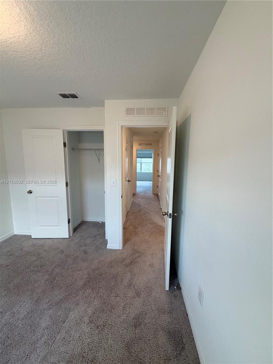 Interior space featuring neutral wall tones, wall-to-wall carpeting, and a reach-in closet with integrated shelving Interior space featuring neutral wall tones, wall-to-wall carpeting, and a reach-in closet with integrated shelving