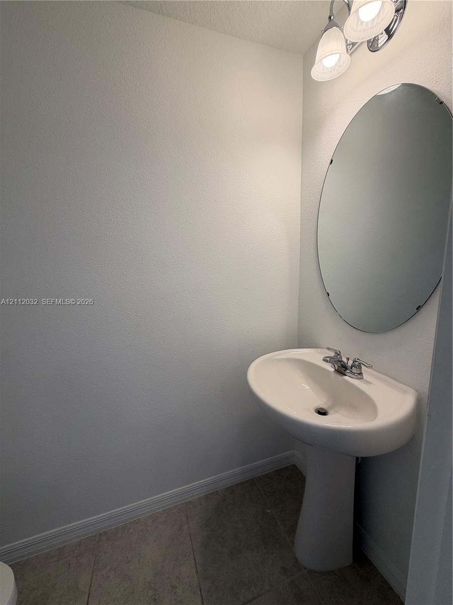 Pedestal sink with a dual-handle faucet, oval frameless wall mirror, and dual-globe light fixture