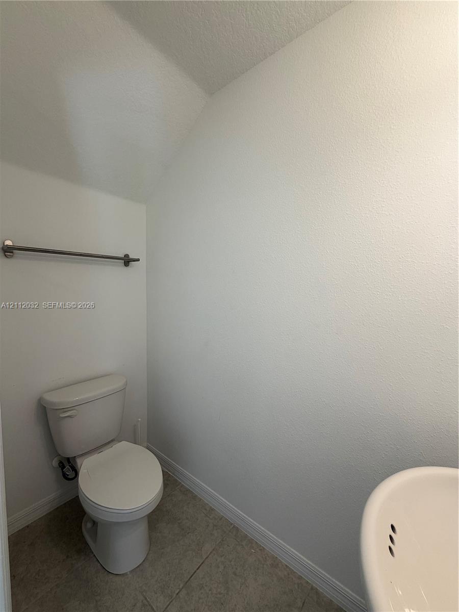 Powder room featuring a ceramic toilet, neutral tile flooring, and a wall-mounted metal towel bar