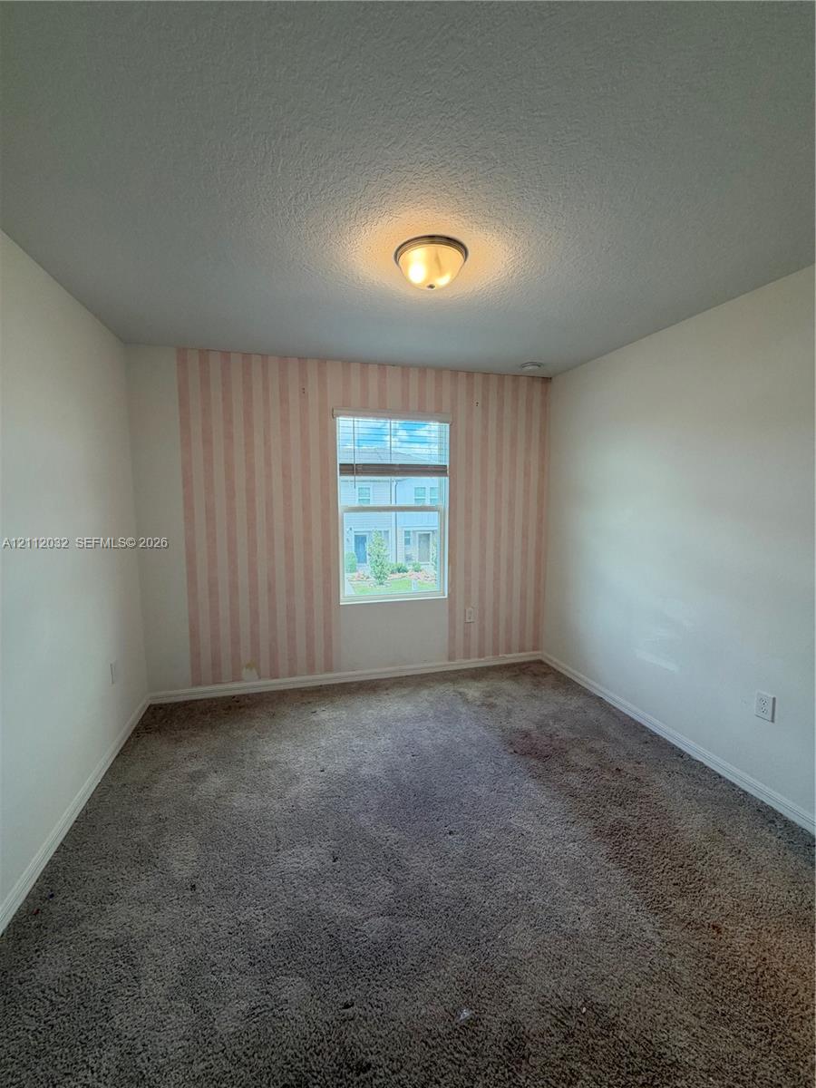 Room featuring carpeting, a single window with horizontal blinds, and a decorative striped accent wall Room featuring carpeting, a single window with horizontal blinds, and a decorative striped accent wall