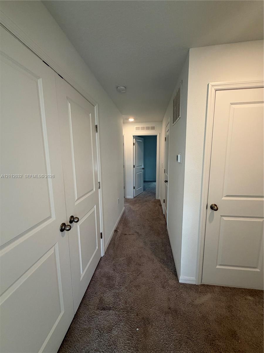 Hallway featuring neutral-toned carpeting, multi-panel doors with round hardware, and recessed lighting