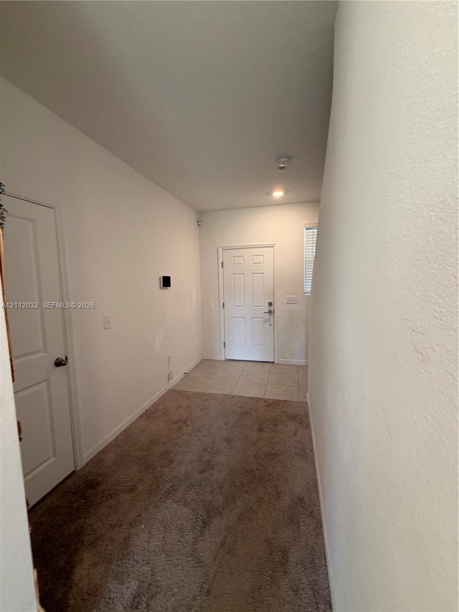 Entryway featuring a white paneled front door, neutral wall-to-wall carpeting, and light-toned ceramic tile flooring