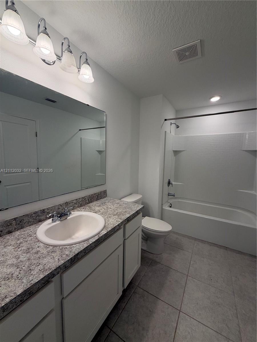 Bathroom featuring a vanity with stone-patterned countertop, oval under-mount sink, full-width wall mirror, four-bulb vanity light, and a tub-shower combination with tile surround