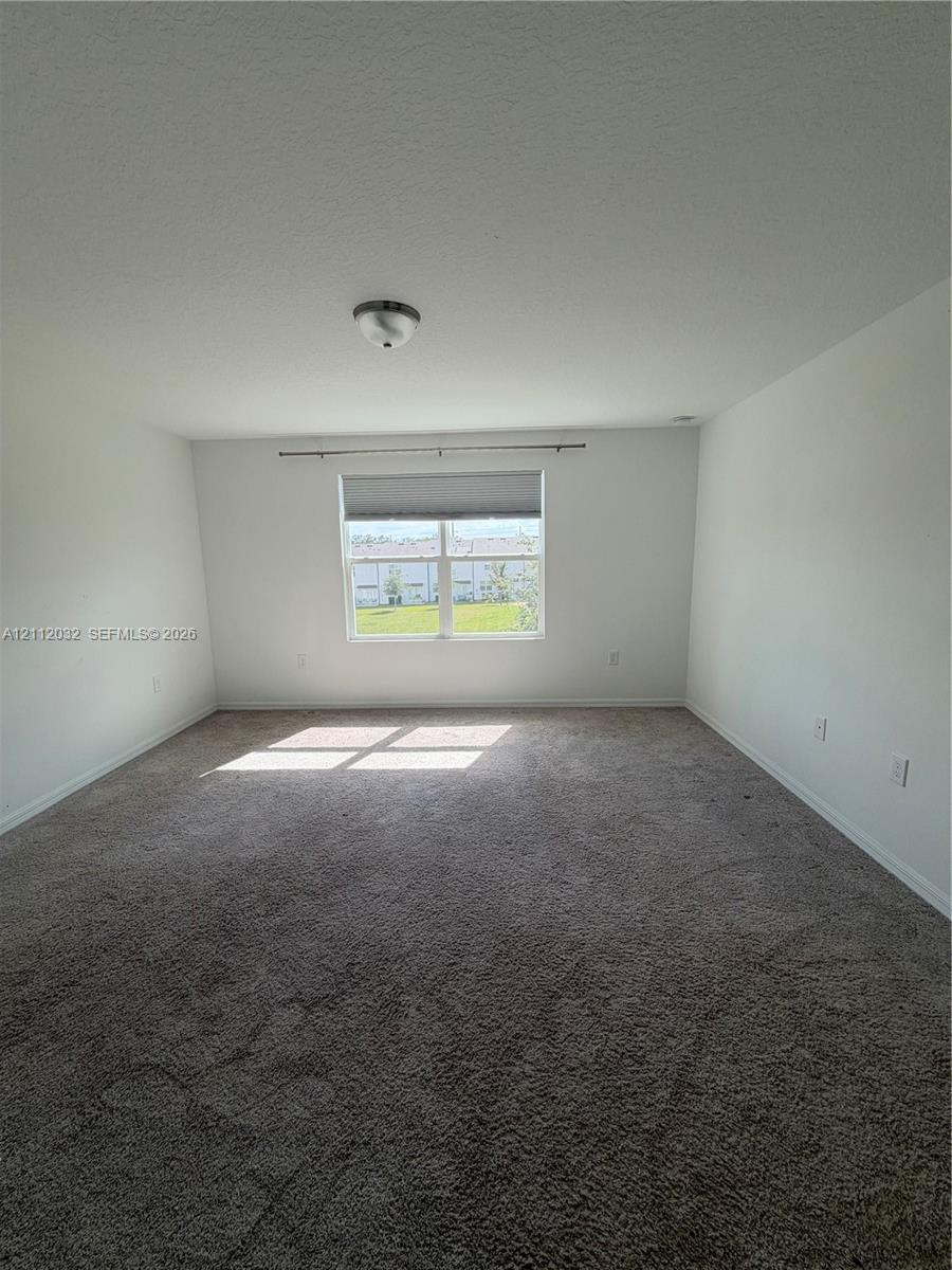 Interior space featuring neutral-toned carpeting, a single-pane window with a roller shade, and a flush-mount ceiling light fixture