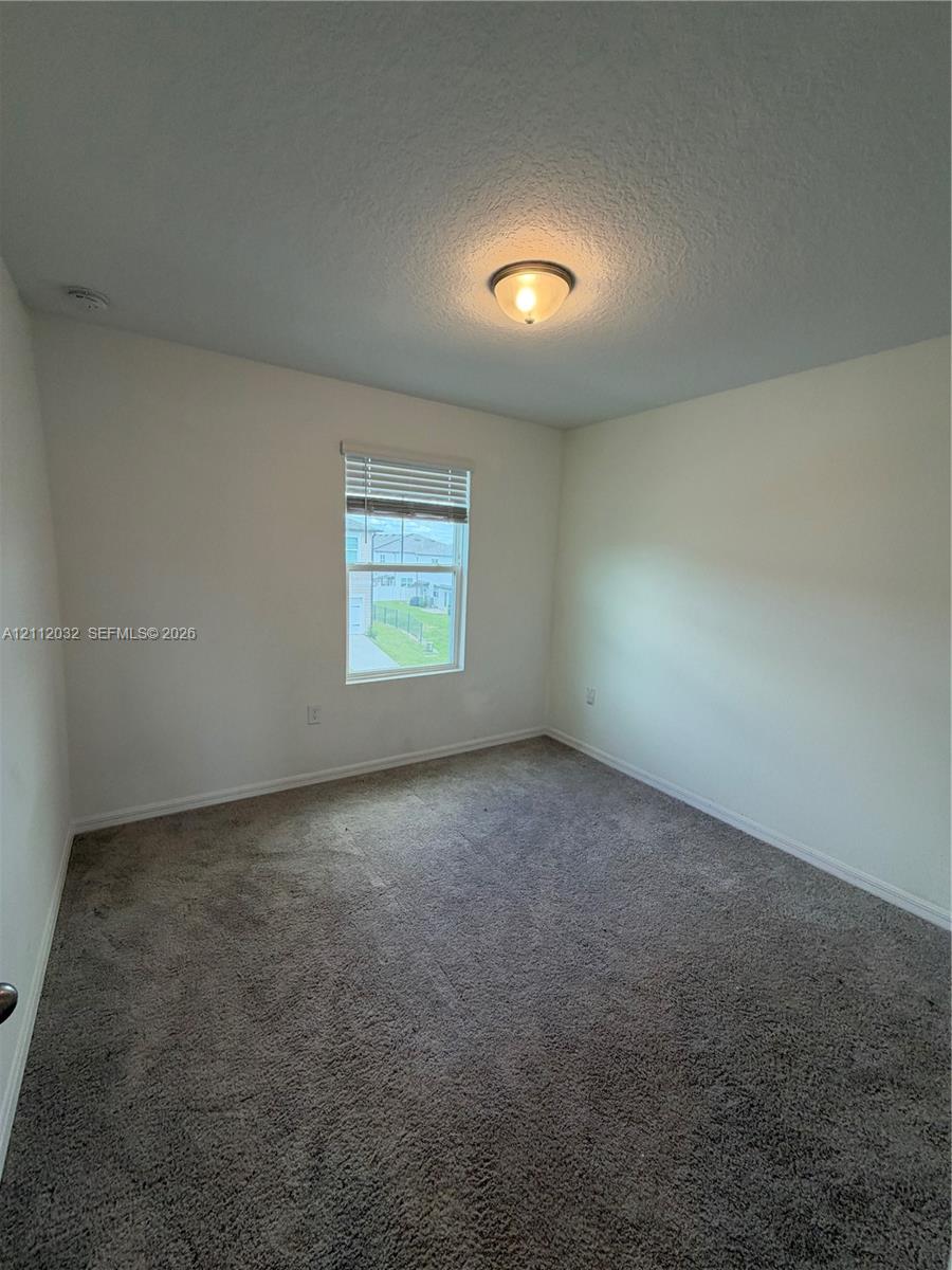 Interior room featuring neutral wall paint, plush carpeting, a single-hung window with horizontal blinds, and a central flush-mount ceiling light fixture Interior room featuring neutral wall paint, plush carpeting, a single-hung window with horizontal blinds, and a central flush-mount ceiling light fixture