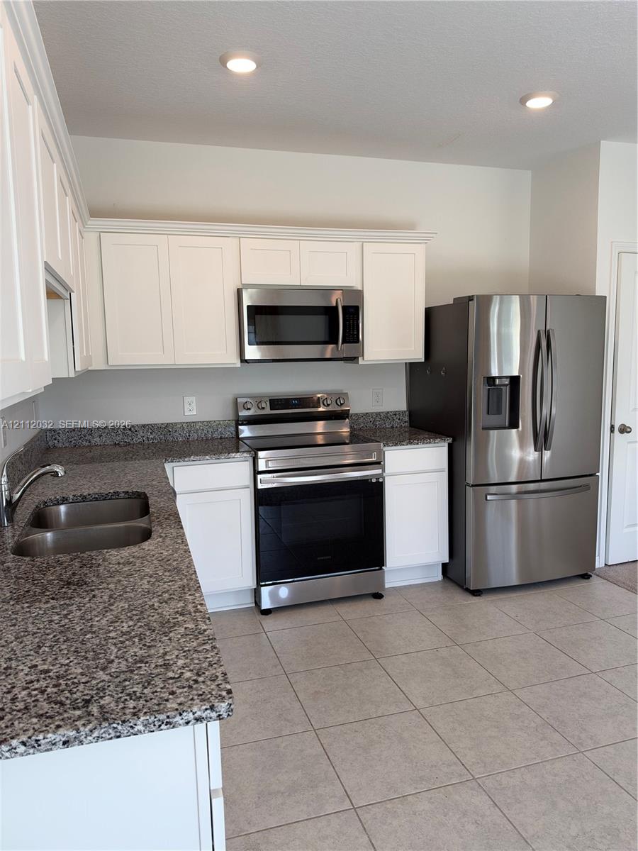 Kitchen featuring white shaker-style cabinetry, stone-finish countertops, stainless steel appliances, a double-basin undermount sink, and tile flooring