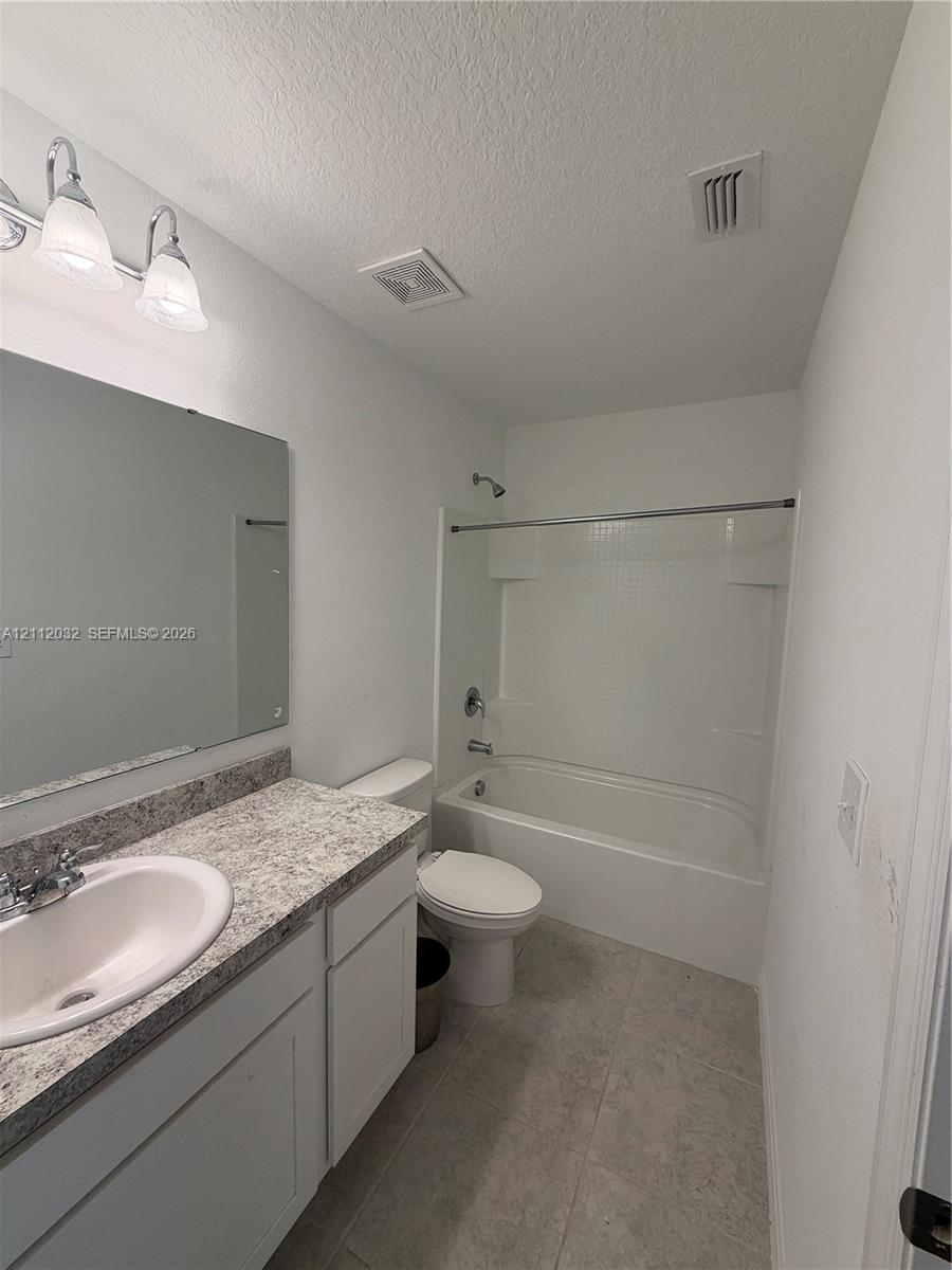 Bathroom featuring a vanity with a stone-finish countertop, integrated sink, and oversized mirror Bathroom featuring a vanity with a stone-finish countertop, integrated sink, and oversized mirror