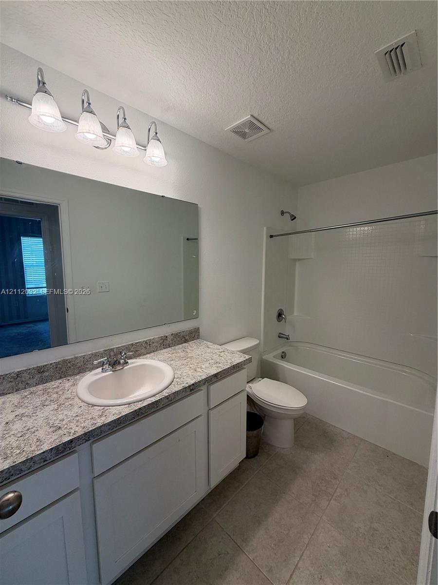 Bathroom featuring a white vanity with a stone-finish countertop, undermount sink, expansive wall mirror, four-light vanity fixture, and a tub-shower combination with tile surround Bathroom featuring a white vanity with a stone-finish countertop, undermount sink, expansive wall mirror, four-light vanity fixture, and a tub-shower combination with tile surround