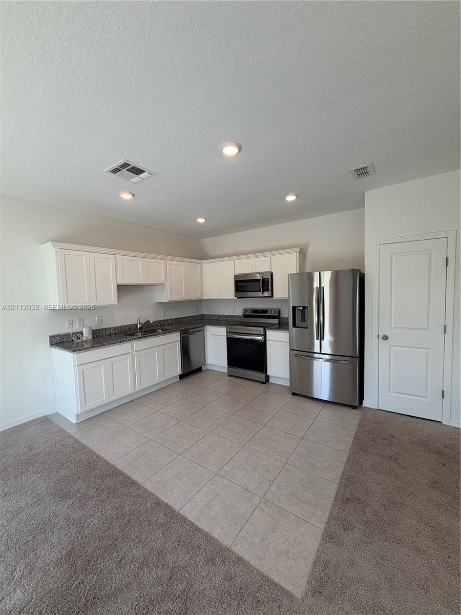 Kitchen featuring white cabinetry, stone-surface countertops, tile flooring, and stainless steel appliances including a refrigerator, range, and microwave