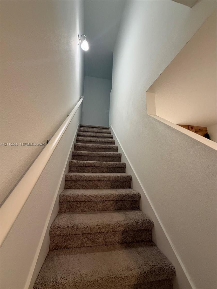 Carpeted staircase featuring a wall-mounted handrail, a sconce lighting fixture, and a recessed wall niche