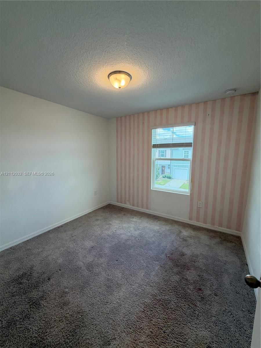 Interior room featuring wall-to-wall carpeting, a single-pane window, flush-mount ceiling lighting, and an accent wall with striped wallcovering Interior room featuring wall-to-wall carpeting, a single-pane window, flush-mount ceiling lighting, and an accent wall with striped wallcovering