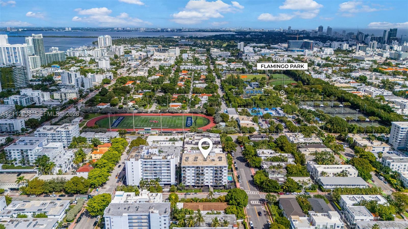 Aerial perspective of a multi-story residential building featuring a swimming pool, flat roof, and proximity to municipal park grounds and athletic facilities