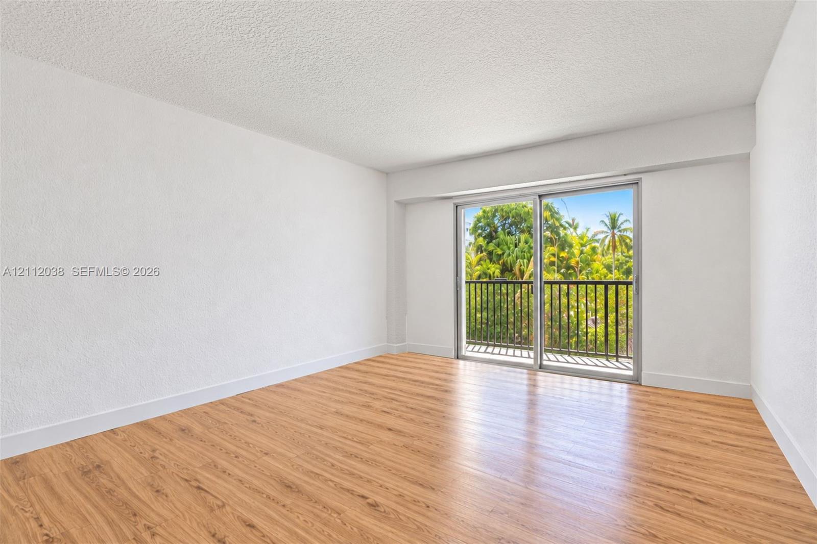 Neutral interior featuring wood-finish flooring, textured ceilings, and a sliding glass door providing access to a balcony with metal railing