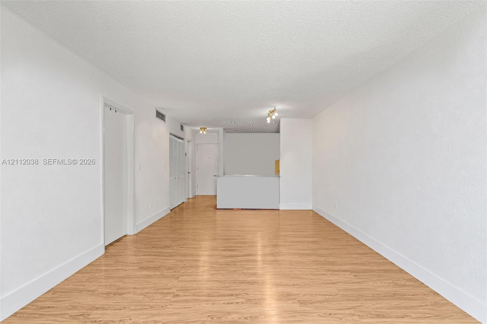 Open interior space featuring wood-finish flooring, textured ceiling, white walls, and built-in closet cabinetry