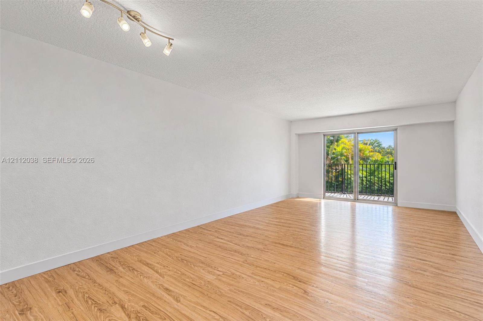Open floor plan featuring wood-finish flooring, textured ceiling, adjustable track lighting, and sliding glass doors with balcony access