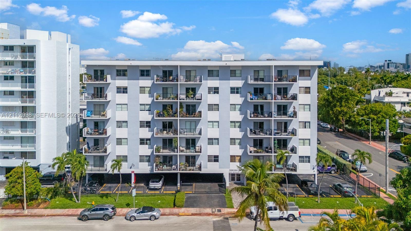 Multi-story residential building featuring reinforced concrete construction, private balconies, covered ground-level parking, and landscaped grounds with mature palm trees