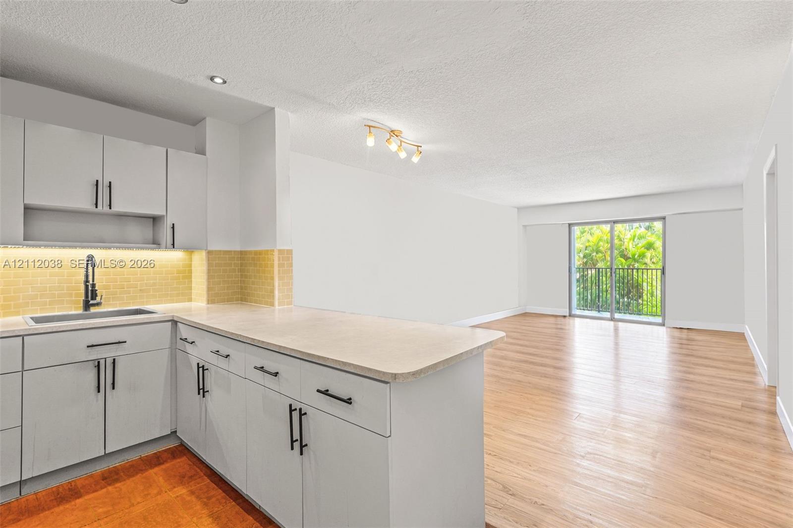 Kitchen featuring light-toned cabinetry, light-toned countertop, subway tile backsplash, and dark hardware
