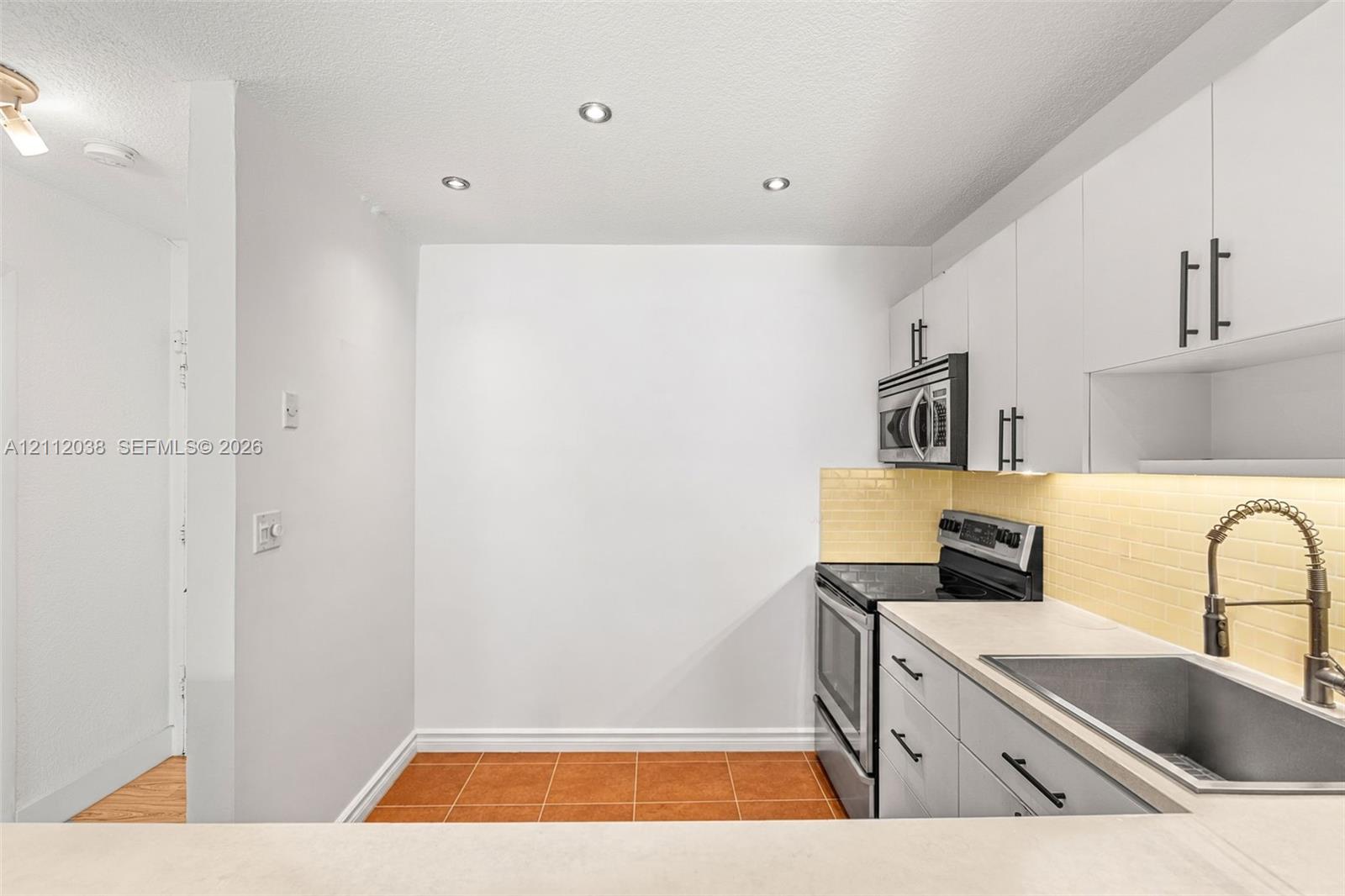 Kitchen featuring white flat-panel cabinetry, stainless steel appliances, a light-toned backsplash, a stainless steel sink with a high-arch faucet, and recessed lighting