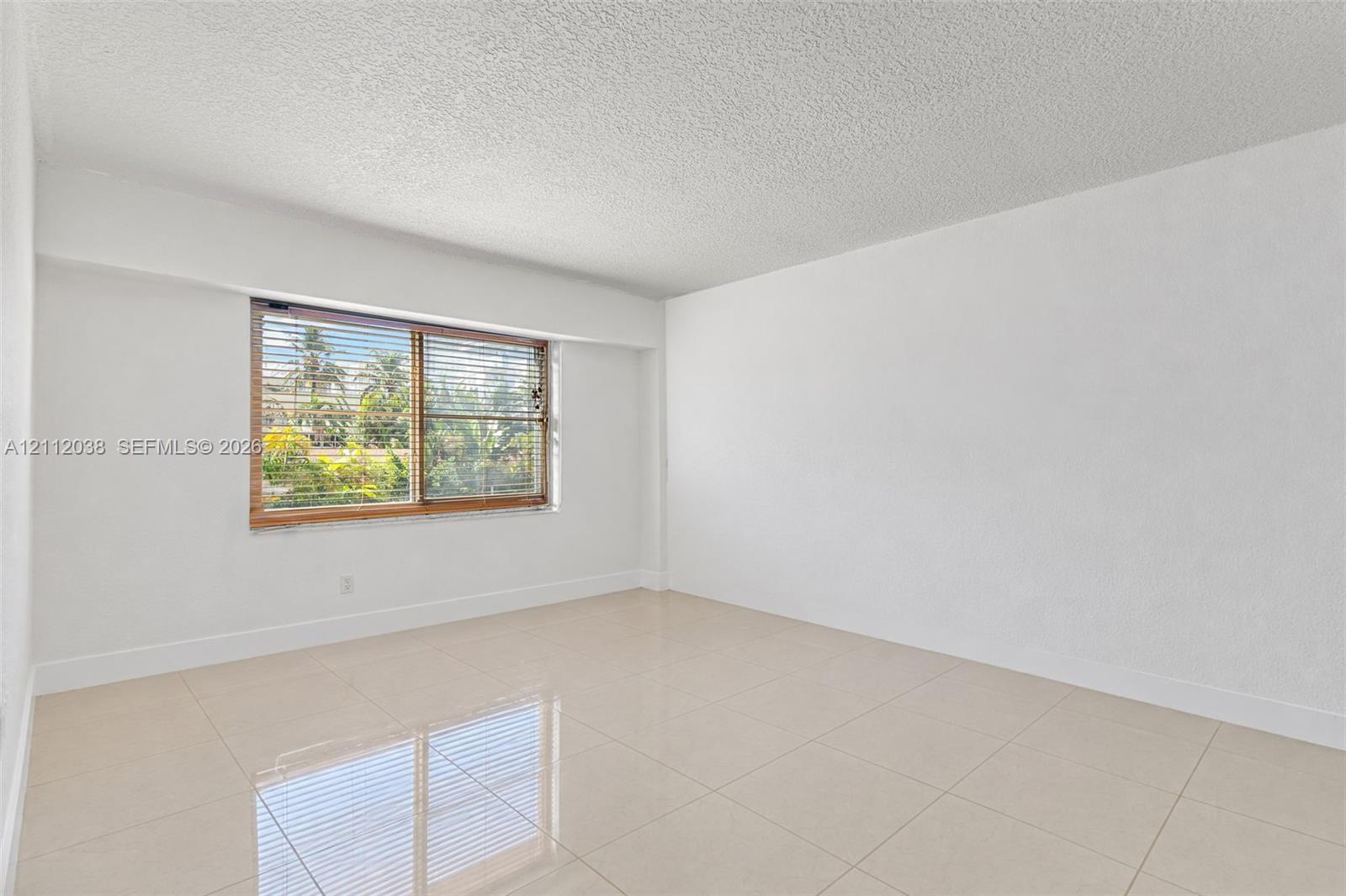 Interior space featuring light-colored tile flooring, smooth wall finishes, a window with integrated blinds, and textured ceiling finish