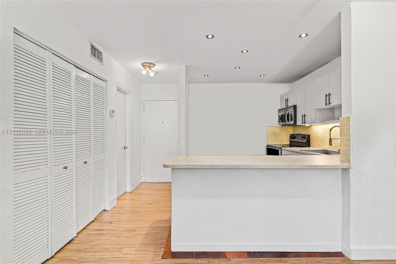 Kitchen featuring white cabinetry, a breakfast bar with stone-finish countertop, under-cabinet lighting, recessed ceiling lighting, and wood-finish flooring