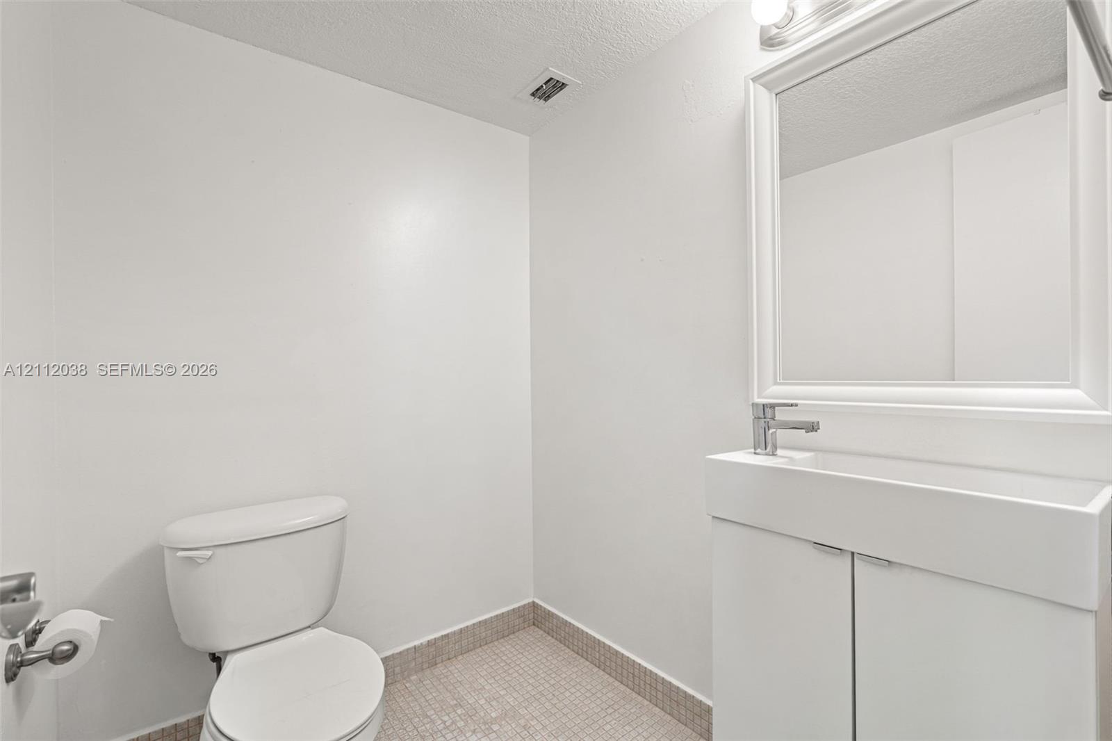 Half-Bathroom featuring a vanity with integrated sink, chrome faucet, framed wall-mounted mirror, and tiled flooring