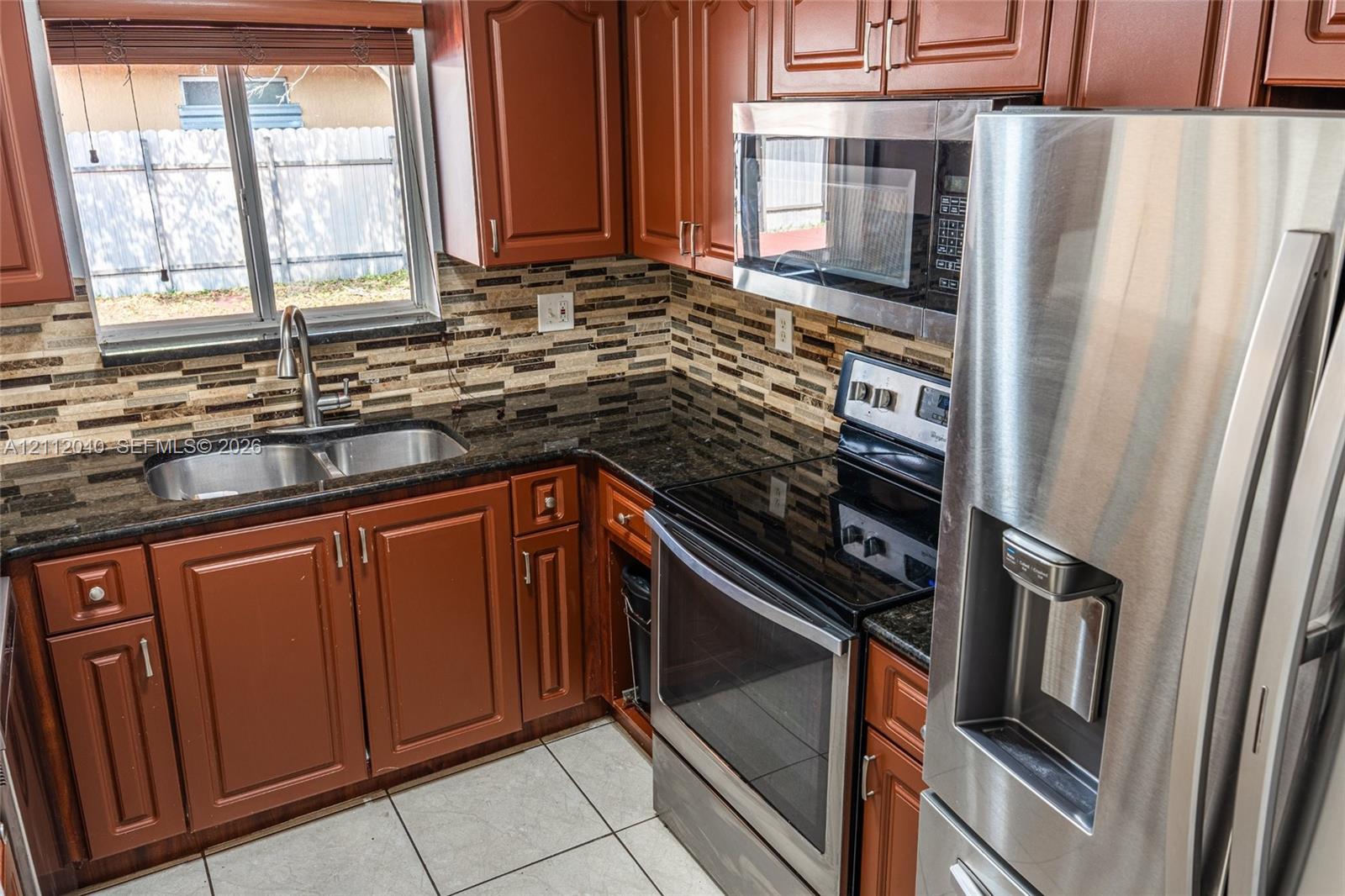 Kitchen featuring raised-panel wood cabinetry, dark stone countertops, stainless steel appliances, a multi-tone tile backsplash, and ceramic floor tile