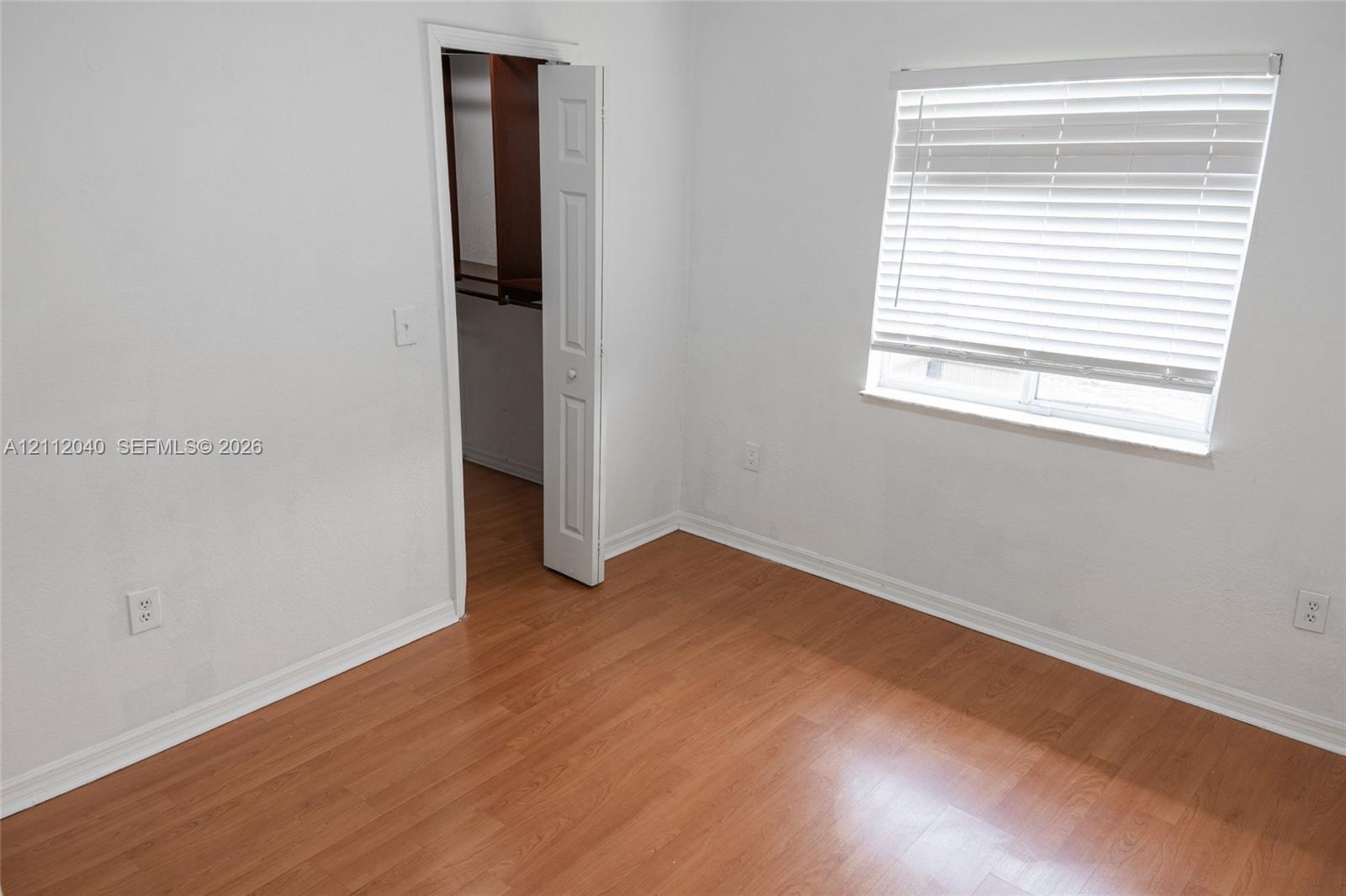 Room featuring wood-finish flooring, white walls, horizontal window blinds, and a closet with a six-panel door