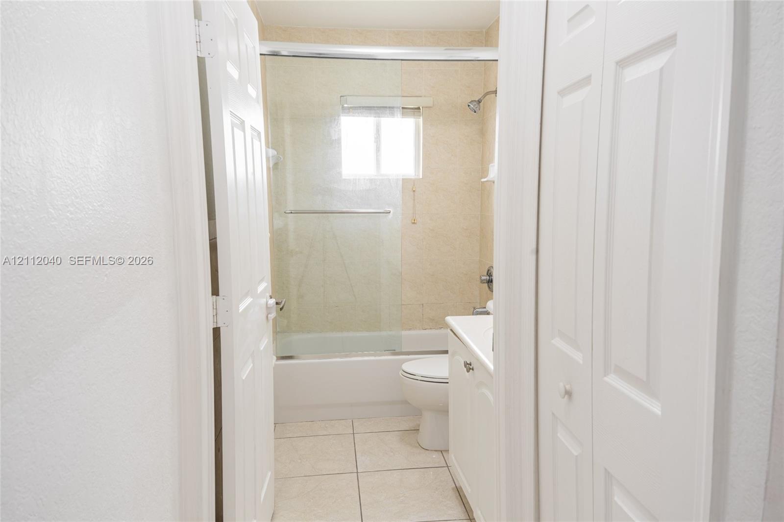 Bathroom featuring a tub-shower combination with a sliding glass enclosure, tile flooring, and a white vanity