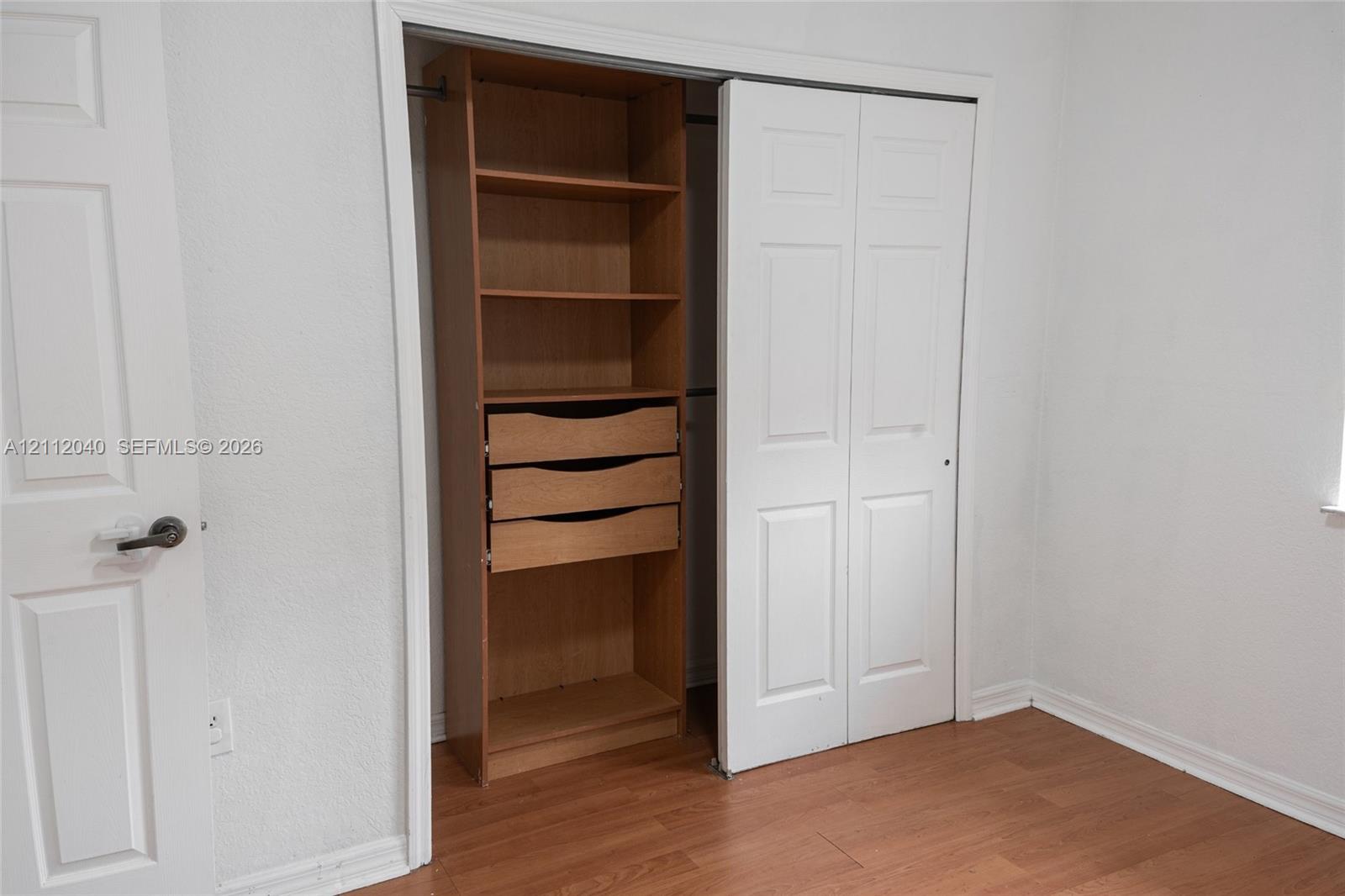 Closet featuring custom wood-finish shelving and integrated storage drawers with white bi-fold doors and wood-finish flooring
