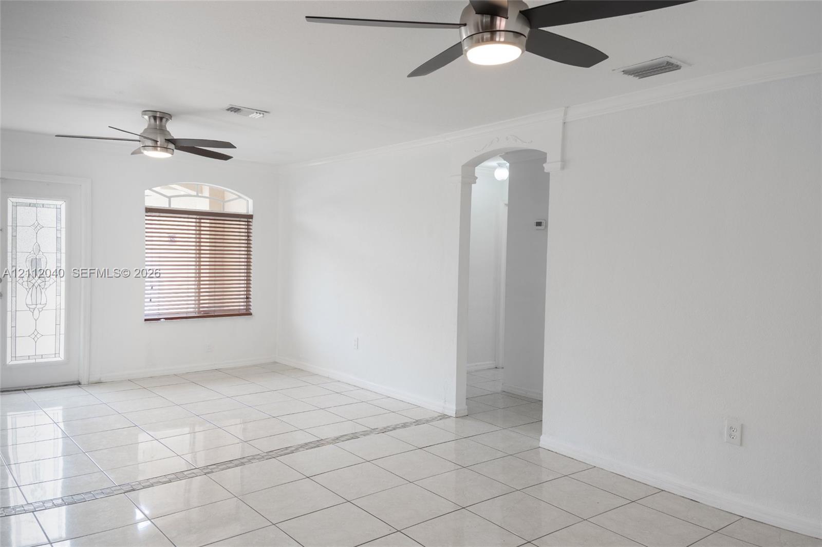 Interior space featuring tile flooring, dual ceiling fans with integrated lighting, an arched doorway, and an exterior door with decorative glass inlay