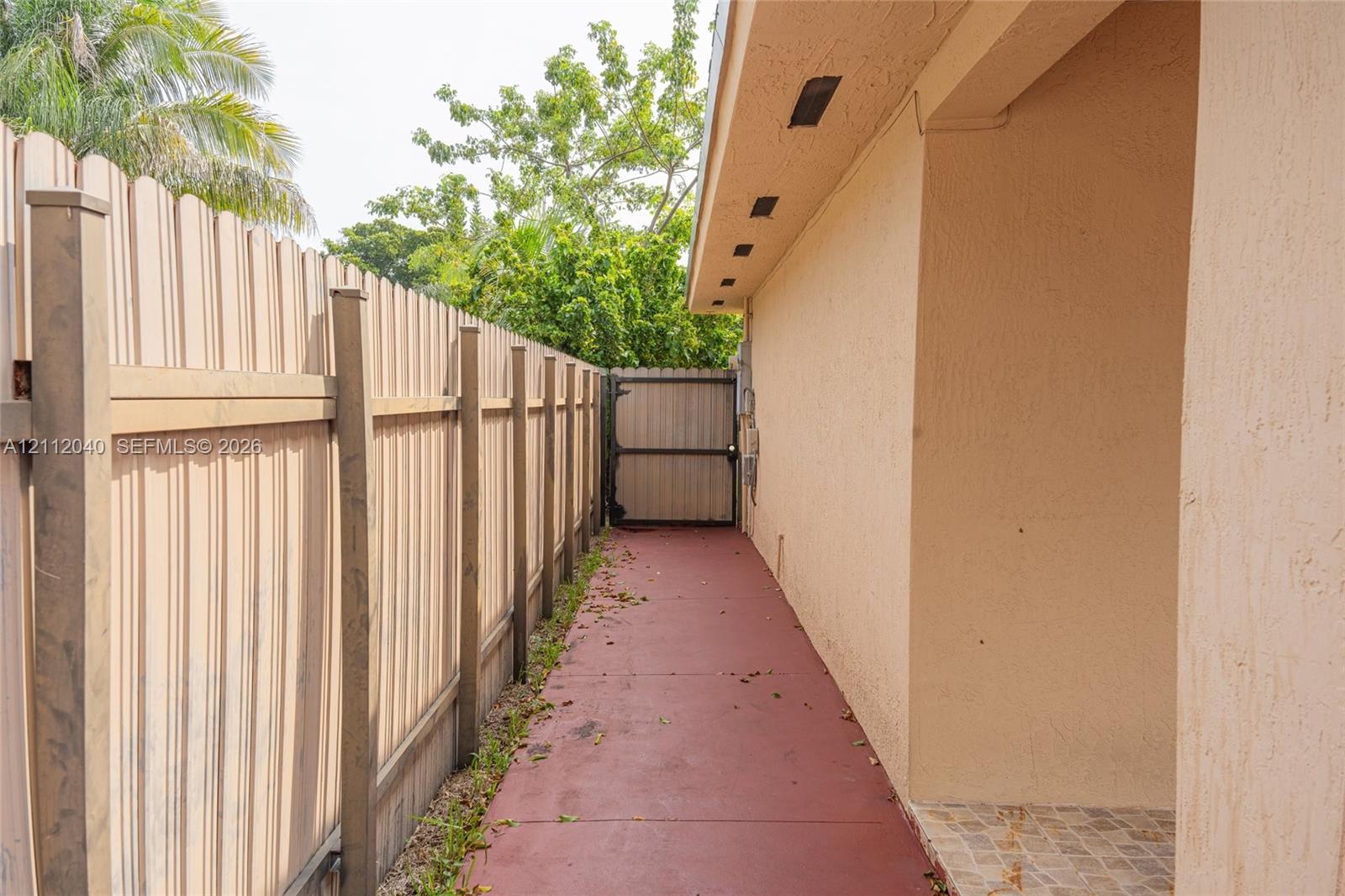 Side exterior walkway featuring a solid vertical fence, gated access, and painted concrete paving