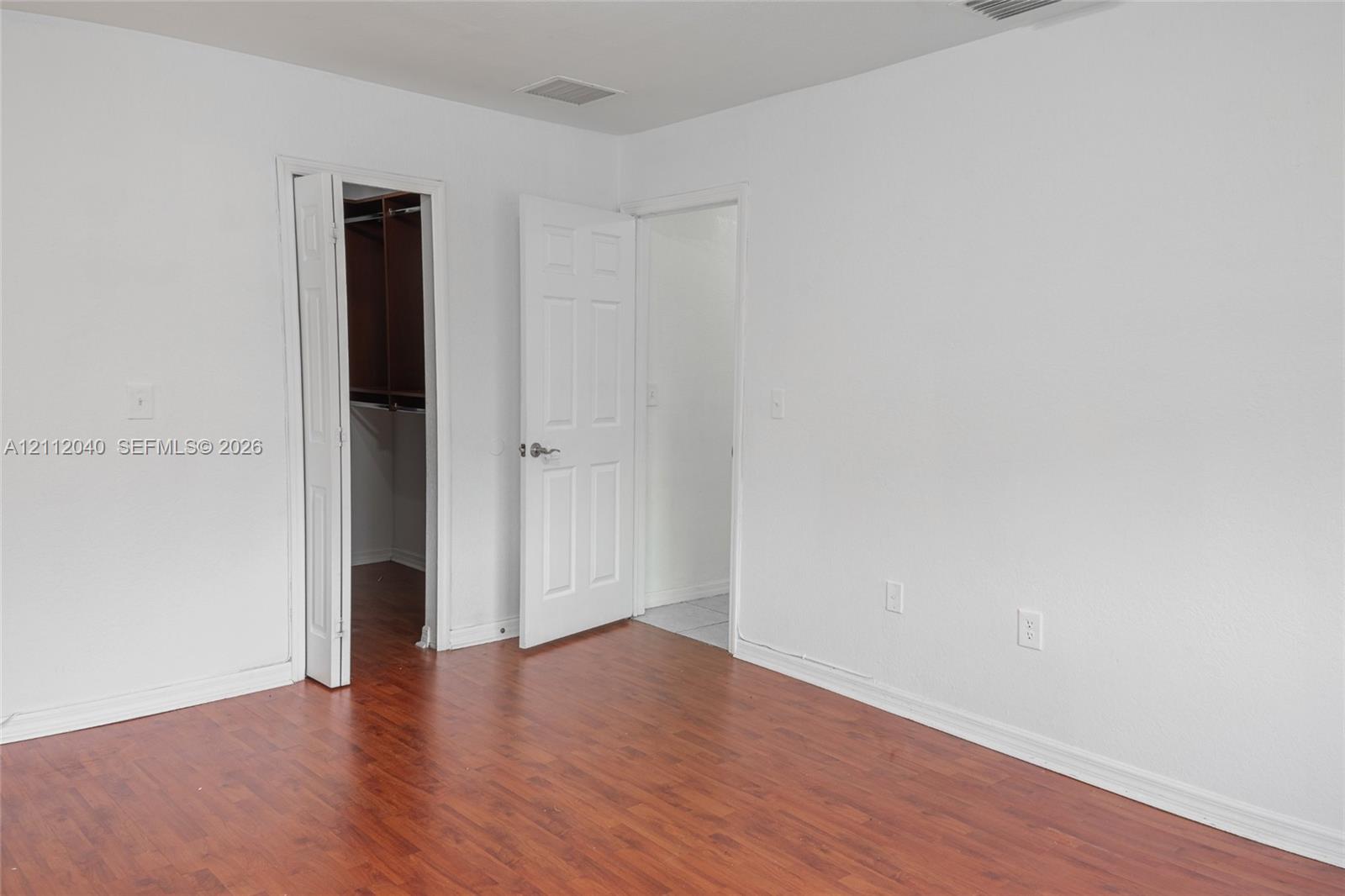 Wood-finish flooring, white paneled interior doors, and a built-in closet with hanging rods