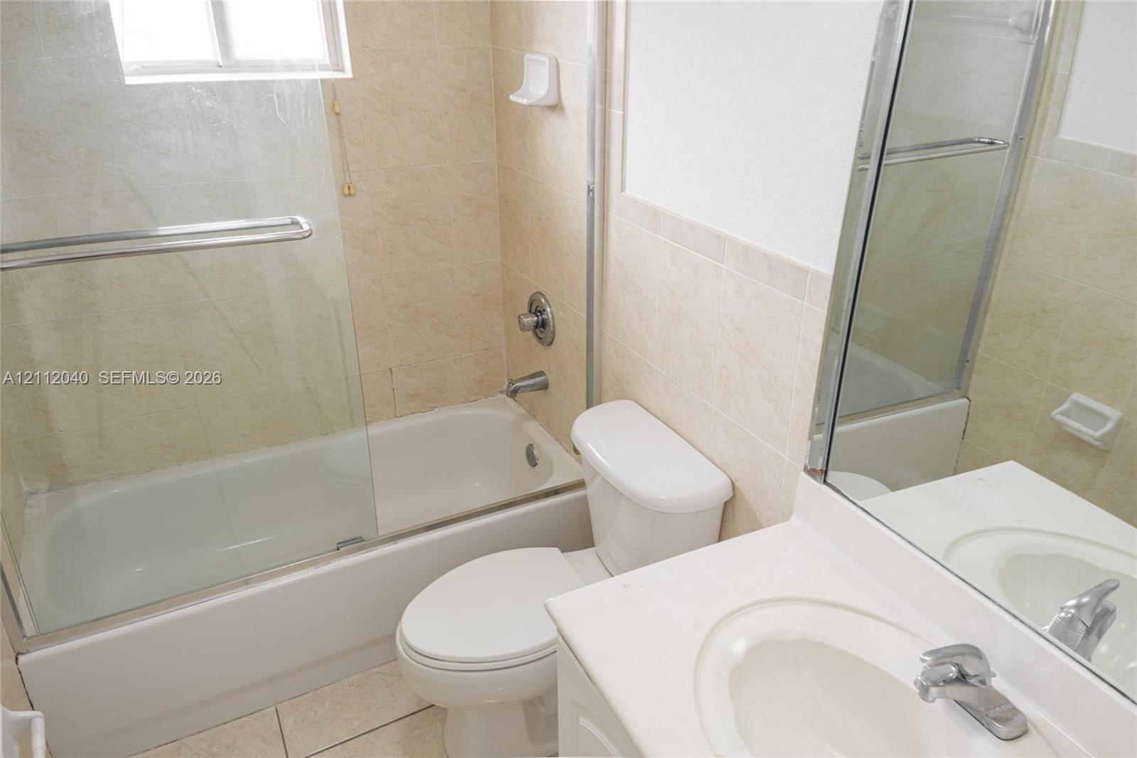 Bathroom featuring neutral tile surround, glass-enclosed bathtub, integrated vanity sink, and polished metal fixtures