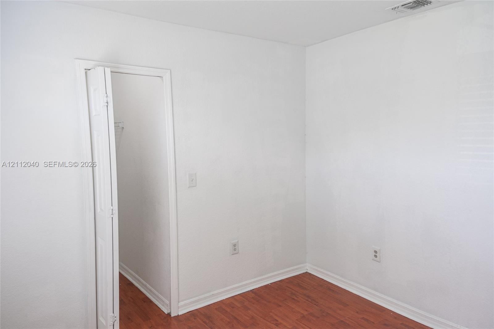 Room featuring wood-finish flooring, white walls, and a bi-fold closet door