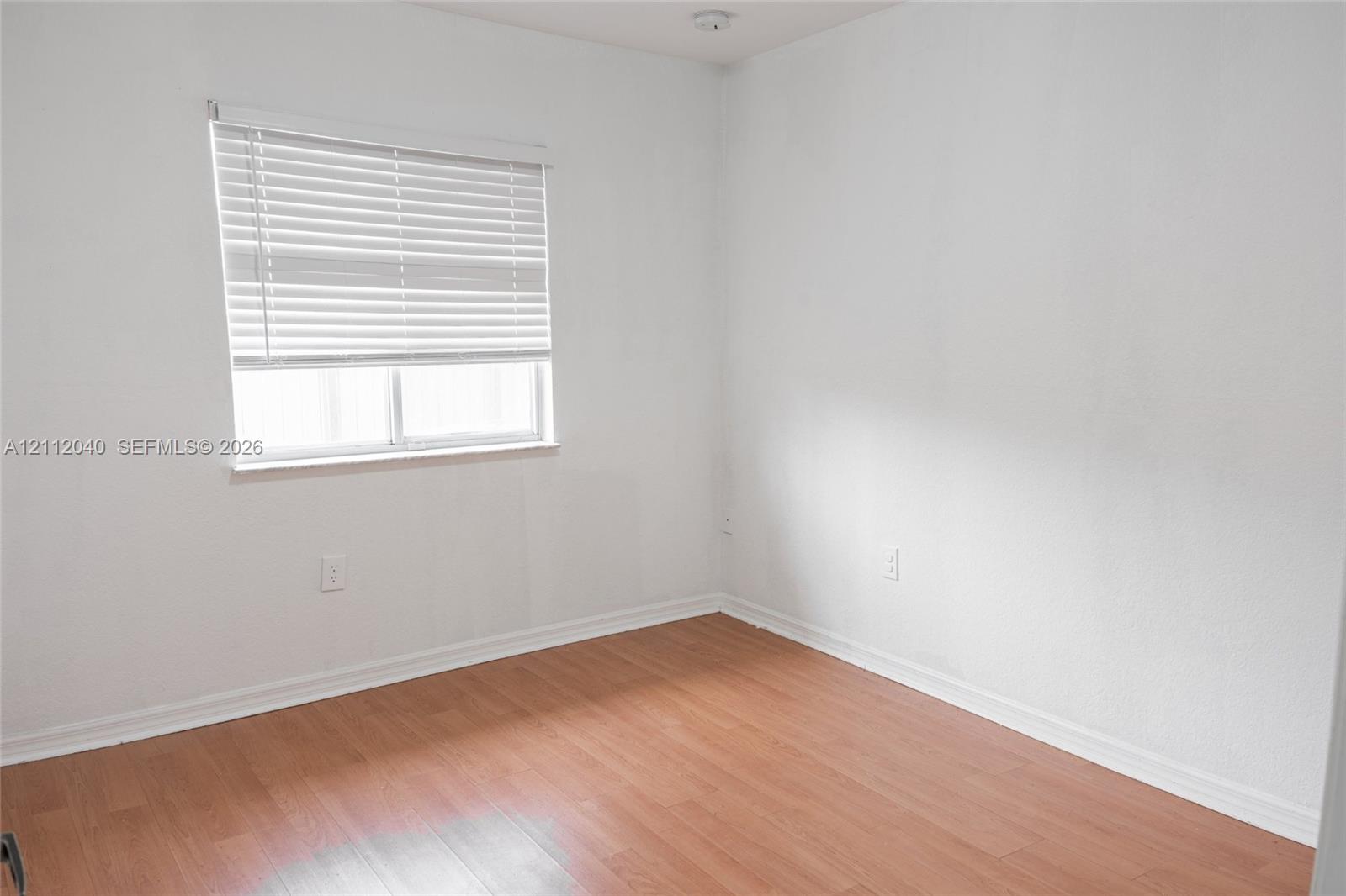 Neutral-toned interior space featuring wood-finish flooring, white walls, and a window with horizontal blinds