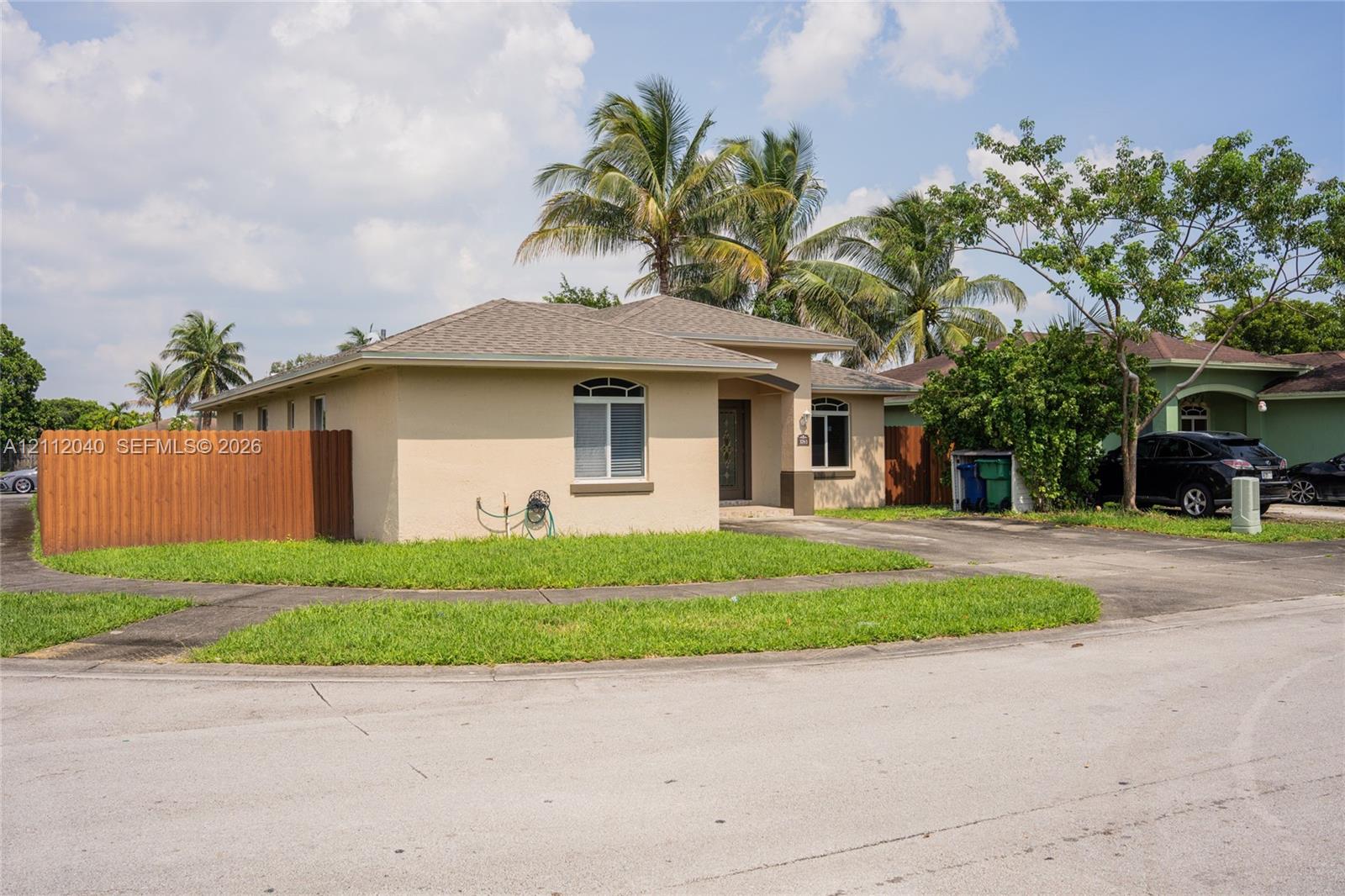Single-story stucco exterior featuring a hipped roof, arched window accents, a concrete driveway, and vertical wood-slat fencing