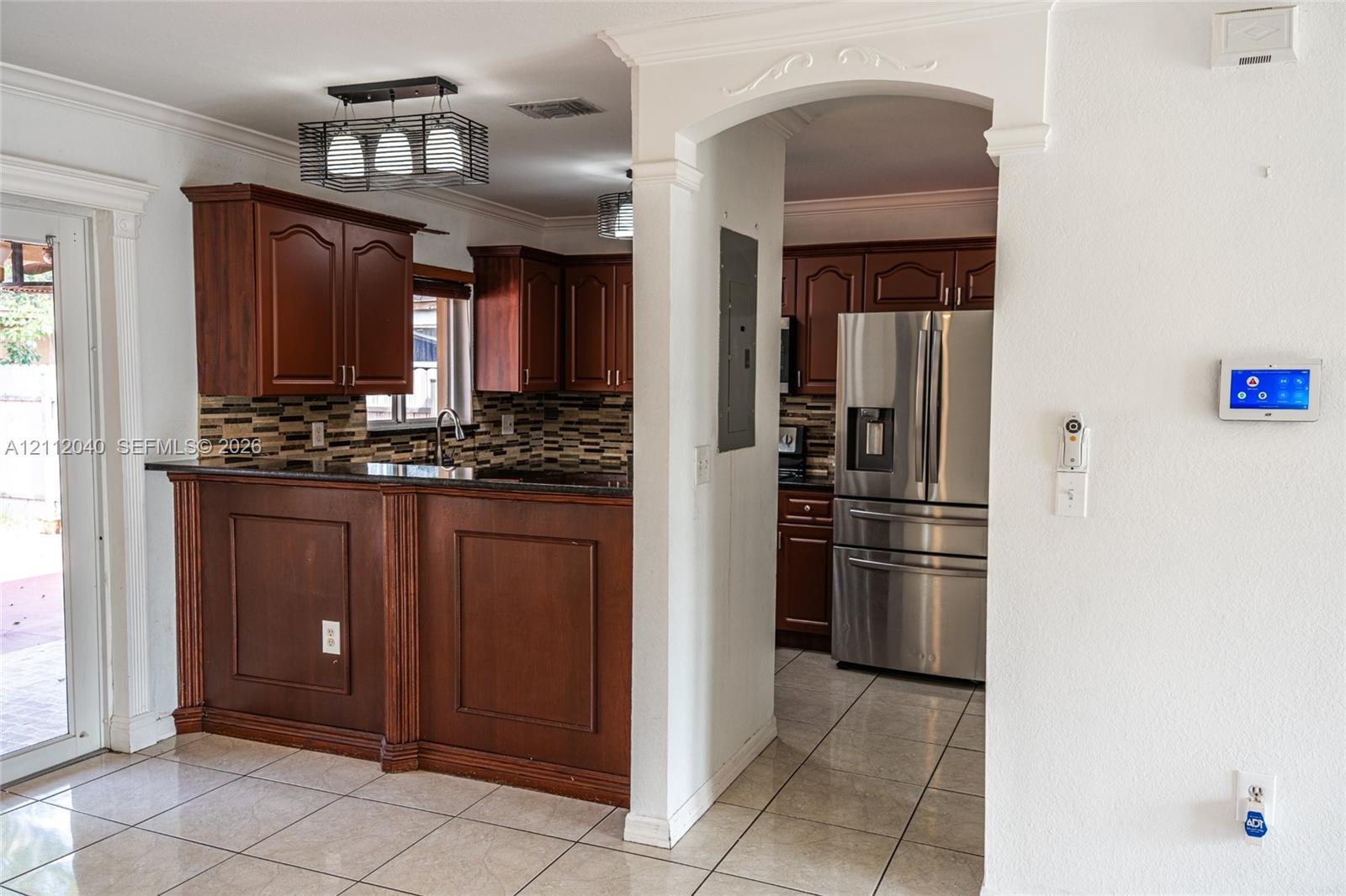 Kitchen featuring wood cabinetry, a peninsula with dark stone countertops, stainless steel appliances, multi-toned tiled backsplash, and ceramic tile flooring