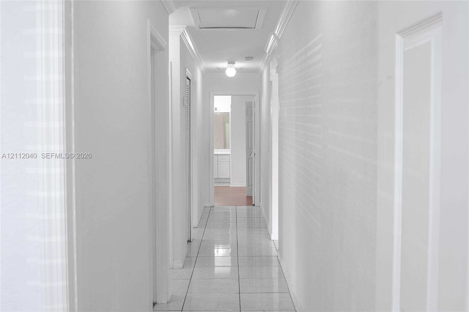 Hallway featuring light-toned tile flooring, crisp neutral wall paint, crown molding, and a flush-mount ceiling fixture