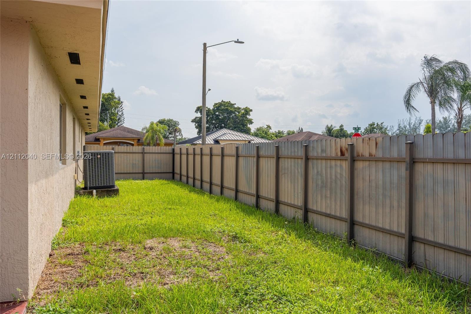 Side yard featuring stucco exterior wall, integrated HVAC condenser unit, and full-height perimeter wood fencing