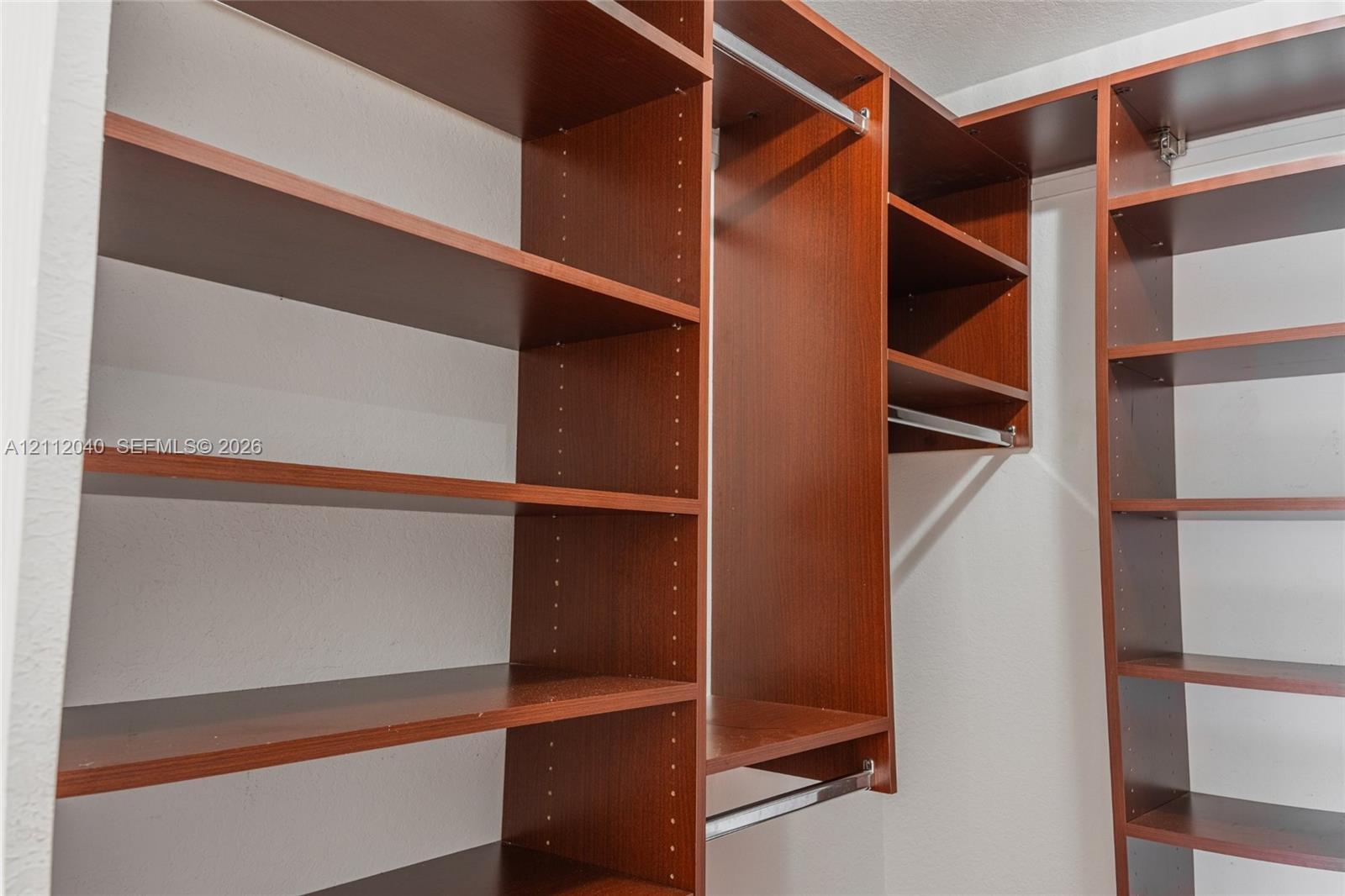 Custom walk-in closet featuring wood-finish cabinetry, adjustable shelving, and integrated metal clothing rods