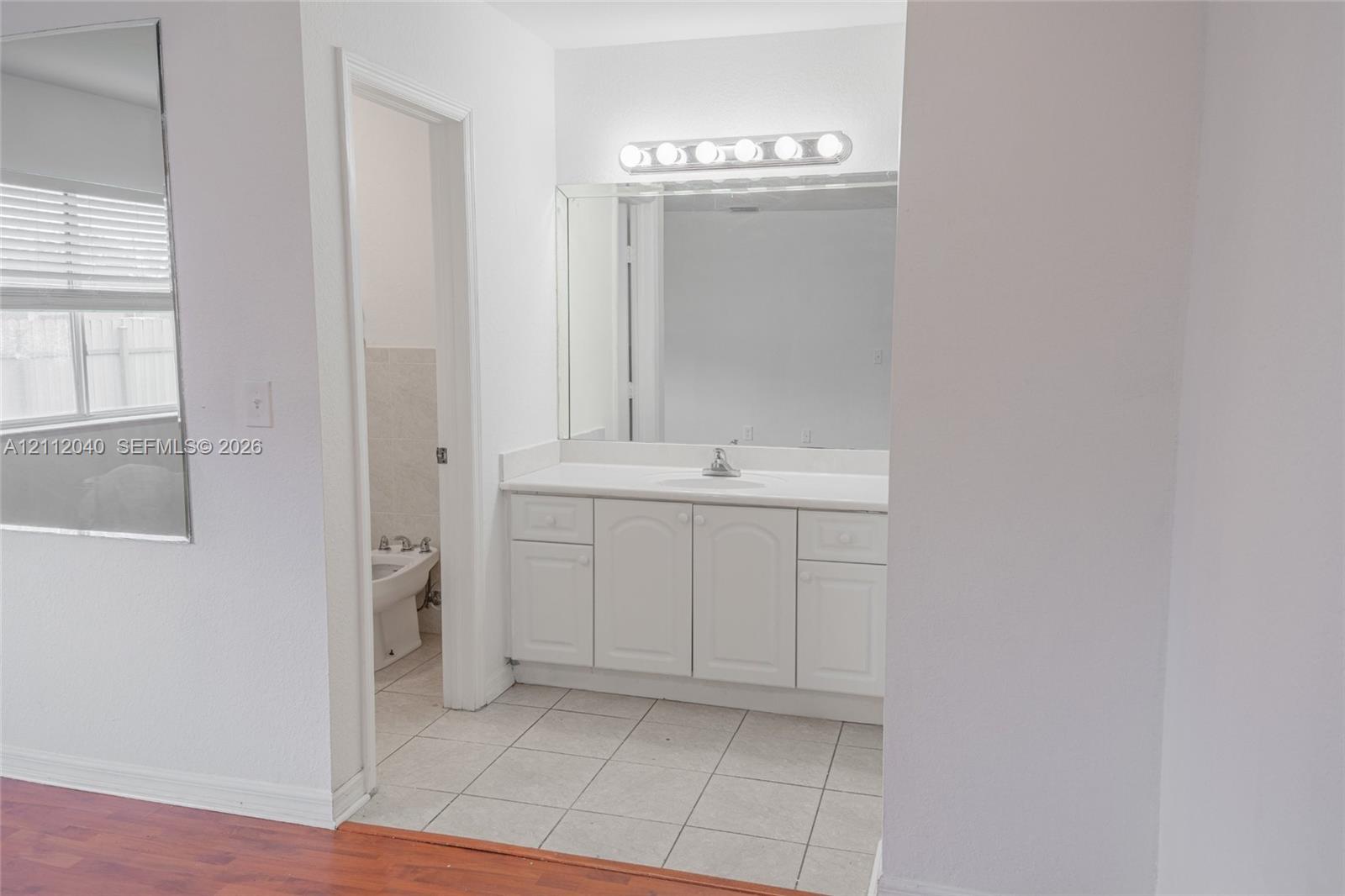 White vanity with storage cabinetry, solid-surface countertop, integrated sink, full-width mirror, and six-bulb vanity lighting