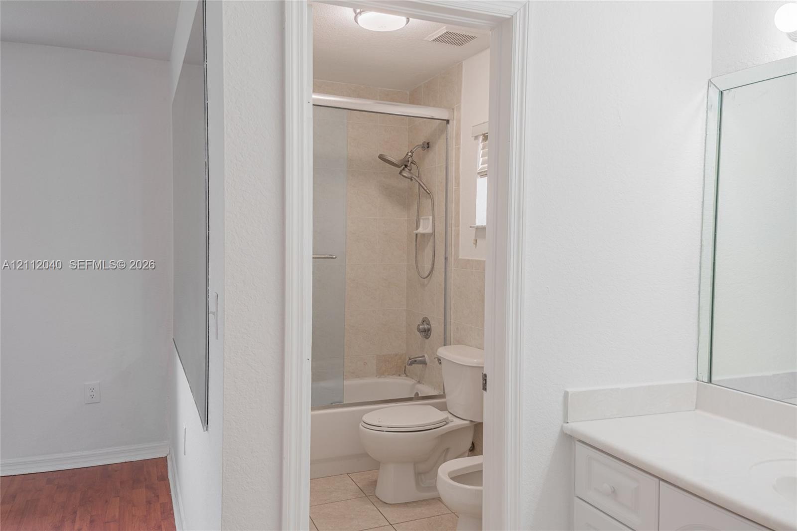 Bathroom featuring white vanity cabinetry with a solid-surface countertop, an expansive wall-mounted mirror, a tub-shower combination with a sliding glass door, and tile flooring