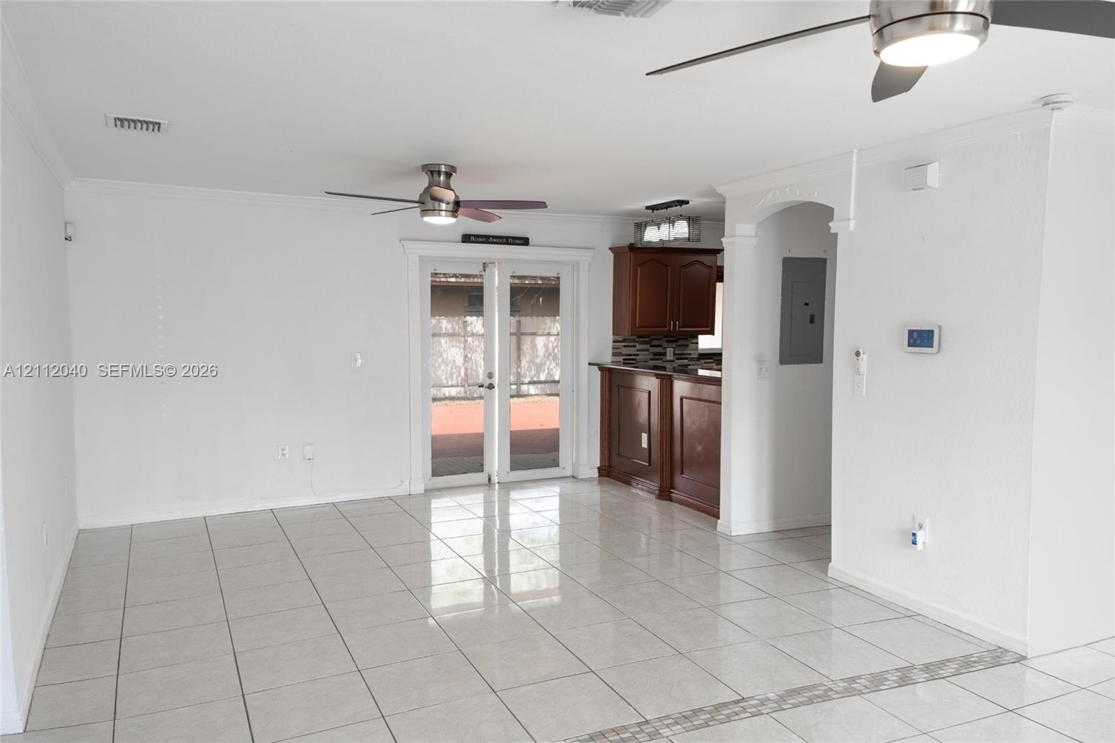 Open-concept interior featuring light-colored tile flooring, dual ceiling fans, French doors, and a kitchen peninsula with dark wood-finish cabinetry
