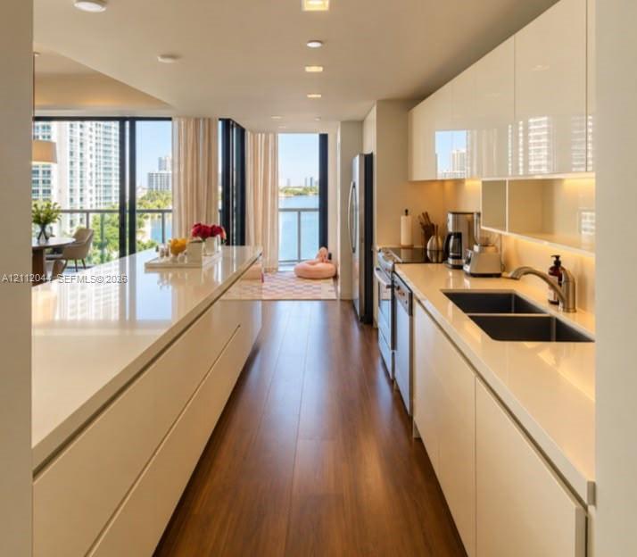 Modern kitchen featuring high-gloss cabinetry, expansive solid-surface countertops, wood-finish flooring, recessed lighting, and stainless steel appliances
