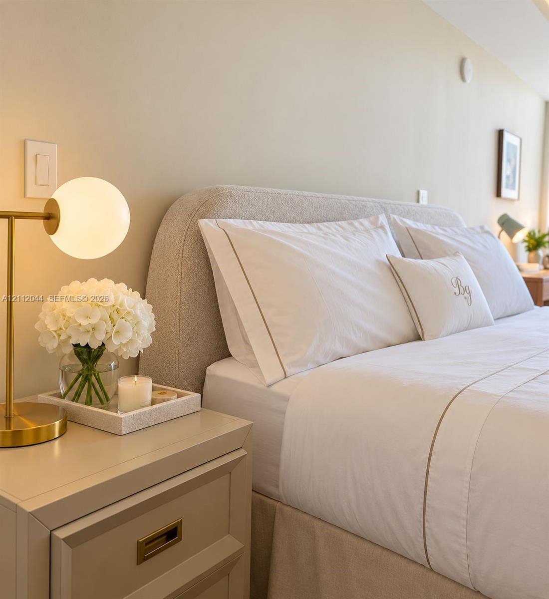 Neutral-toned room featuring a built-in light-colored nightstand with recessed gold-tone hardware and a wall-mounted light switch