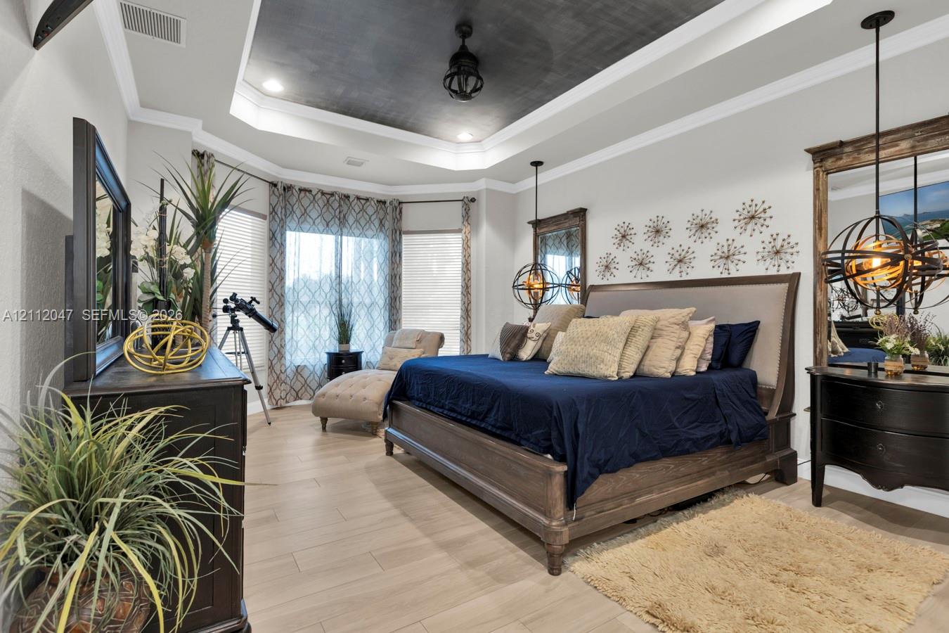 Tray ceiling with dark-toned inlay, wood-finish flooring, bay window configuration, and spherical pendant lighting