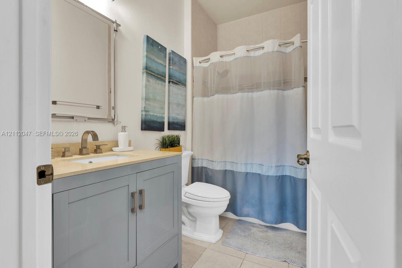 Grey-toned vanity with a stone-surfaced countertop, integrated under-mount sink, brushed-metal faucet, and a wall-mounted rectangular mirror